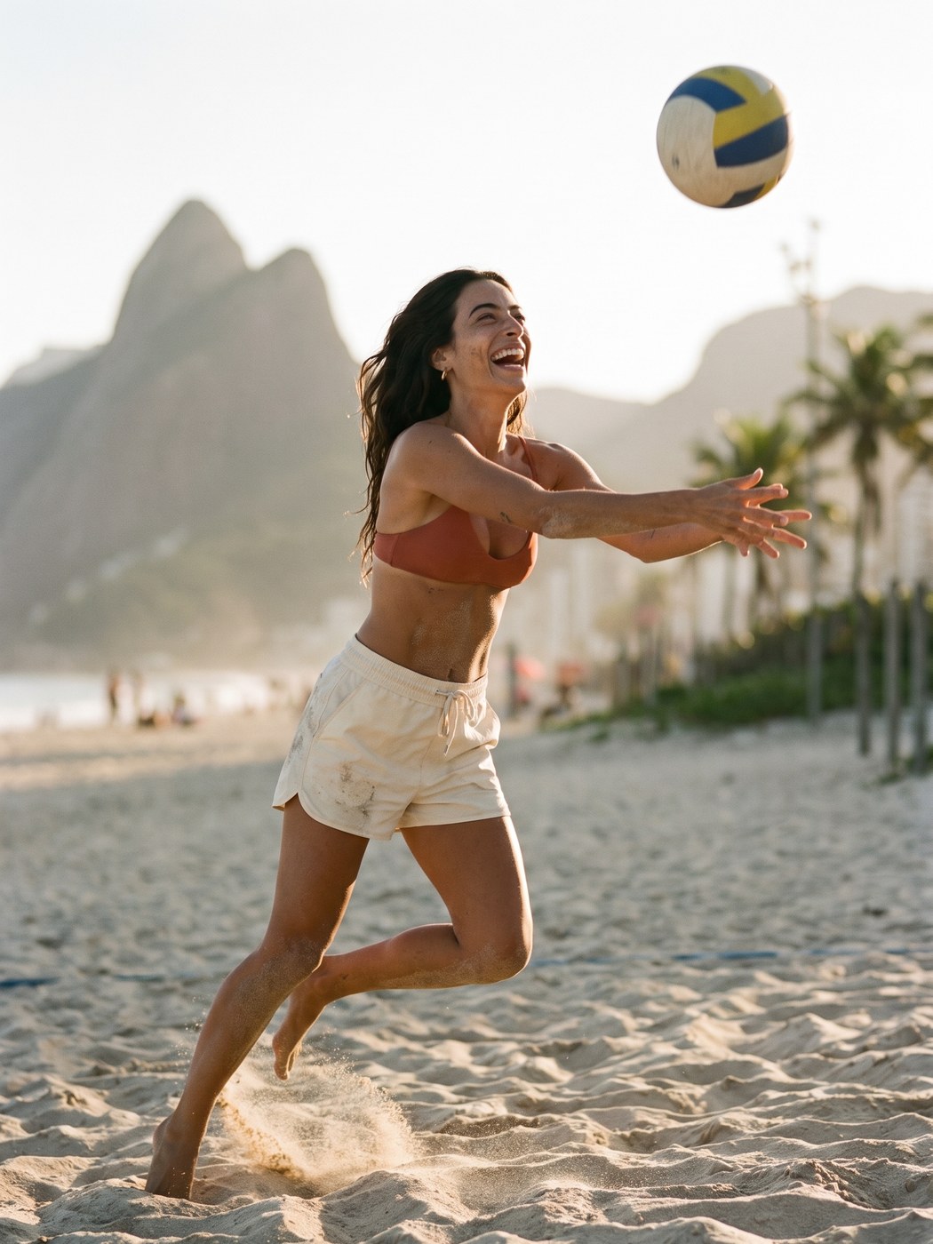 Mulher rindo enquanto joga vôlei na praia ao pôr do sol, com o Dois Irmãos ao fundo.